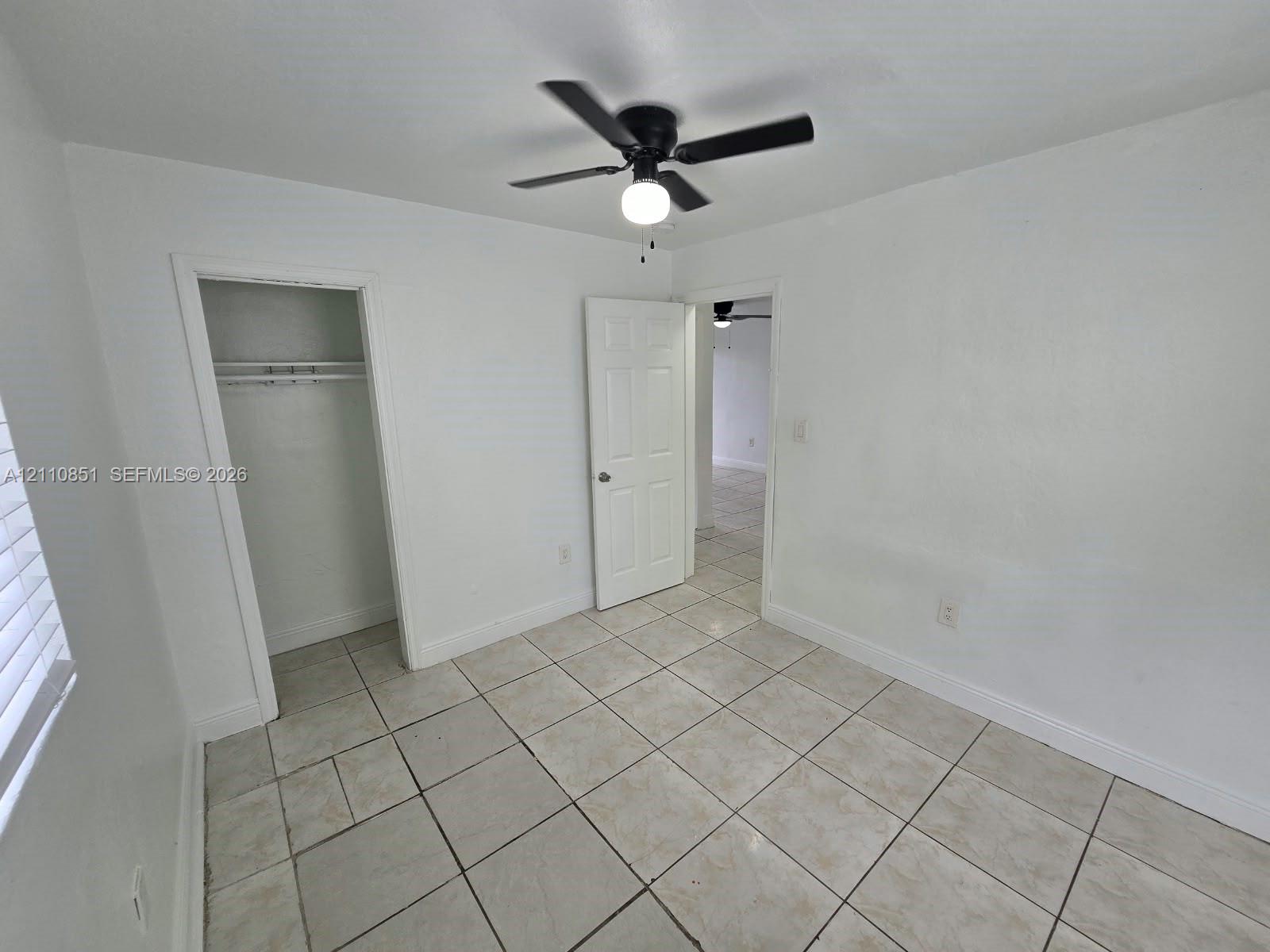 Room featuring light-toned tile flooring, a matte black ceiling fan with an integrated light fixture, a six-panel interior door, and a built-in closet with an overhead shelf