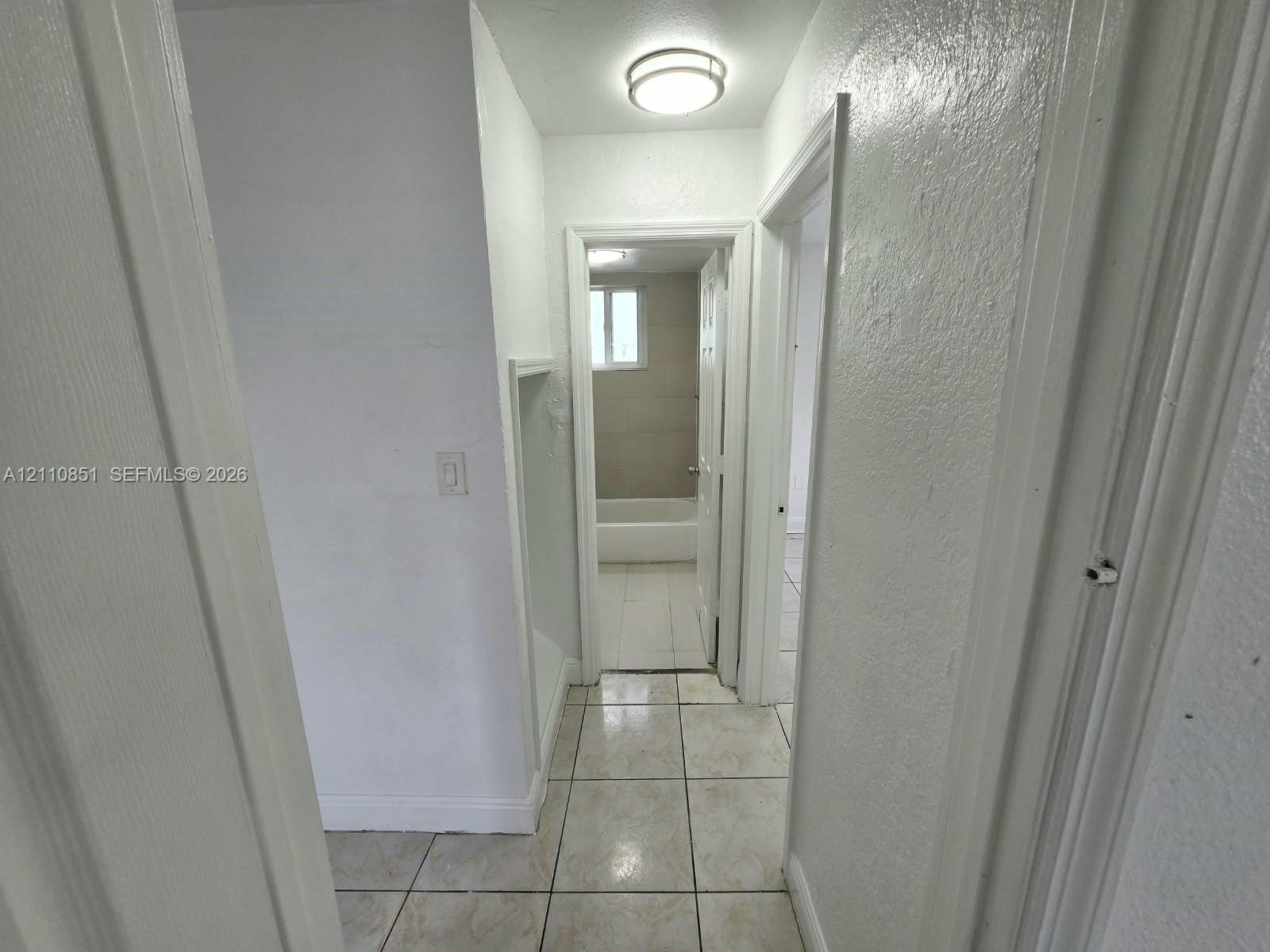 Hallway featuring neutral tile flooring, smooth-finish walls, and a recessed wall niche