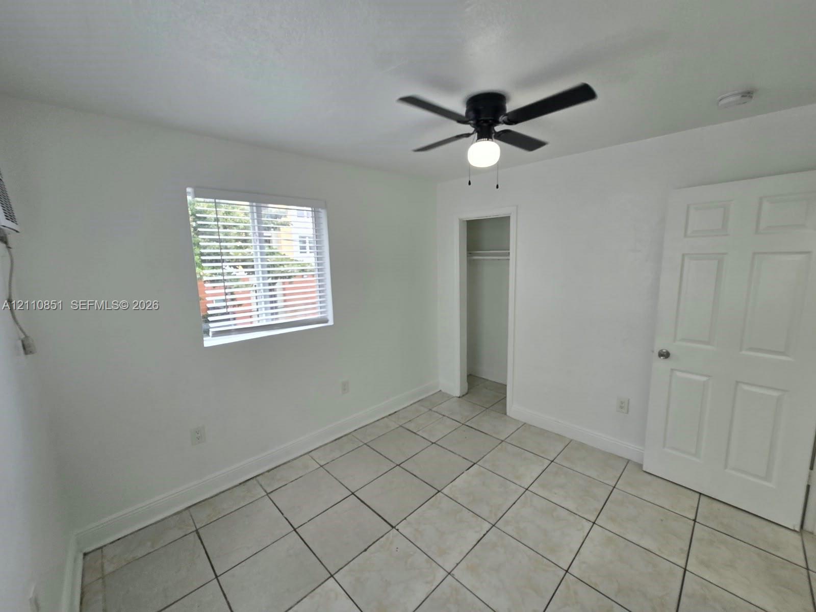 Room featuring tile flooring, a window with horizontal blinds, a ceiling fan with light fixture, a closet, and a six-panel door