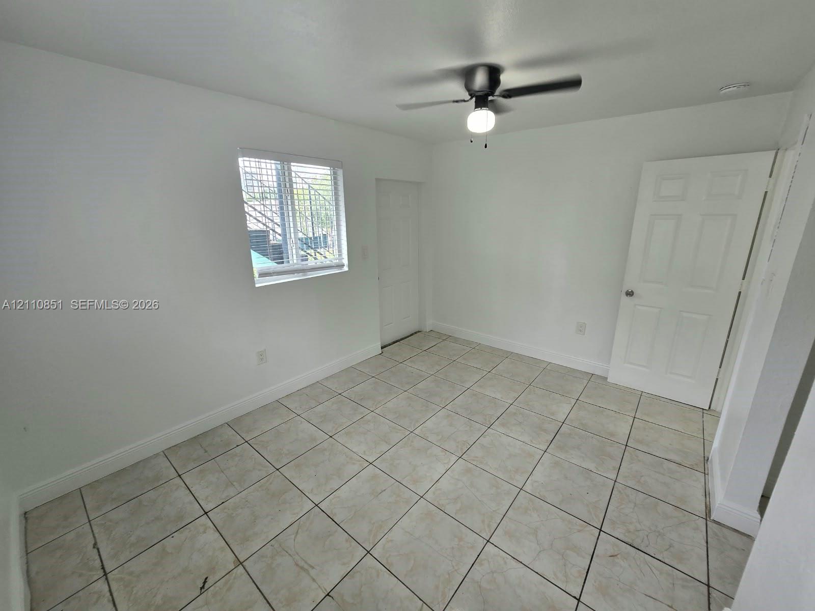 Interior room featuring neutral floor tiling, a multi-panel door, and a ceiling-mounted fan with integrated lighting
