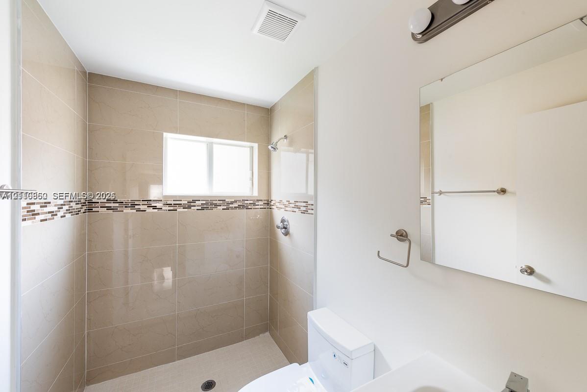 Bathroom featuring a walk-in shower with large-format neutral wall tile, decorative mosaic tile inlay, wall-mounted mirror, and vanity lighting