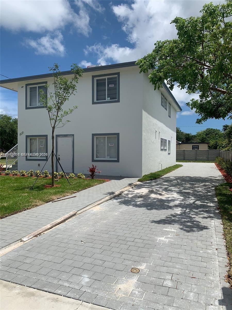 Two-story exterior featuring a smooth stucco finish, gray-framed windows, a brick-paved driveway, and a concrete masonry unit perimeter fence