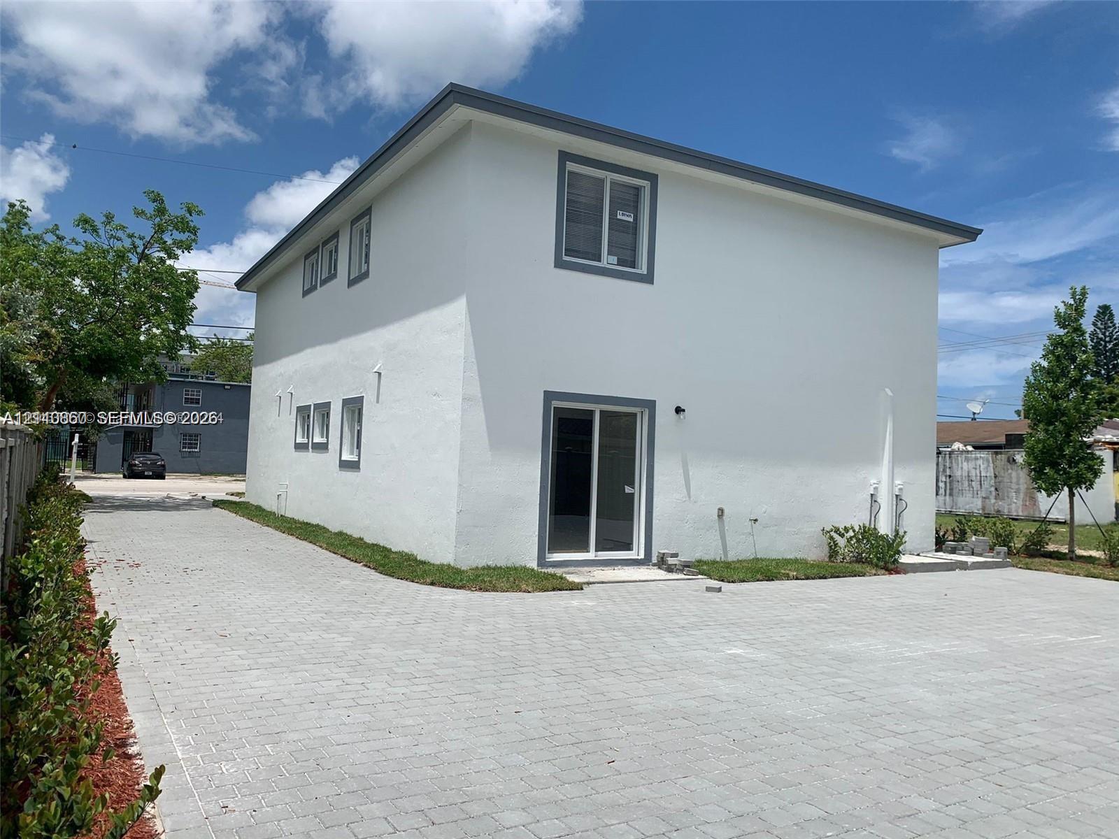 Two-story structure with a smooth stucco exterior, sliding glass door, and a sprawling paved driveway
