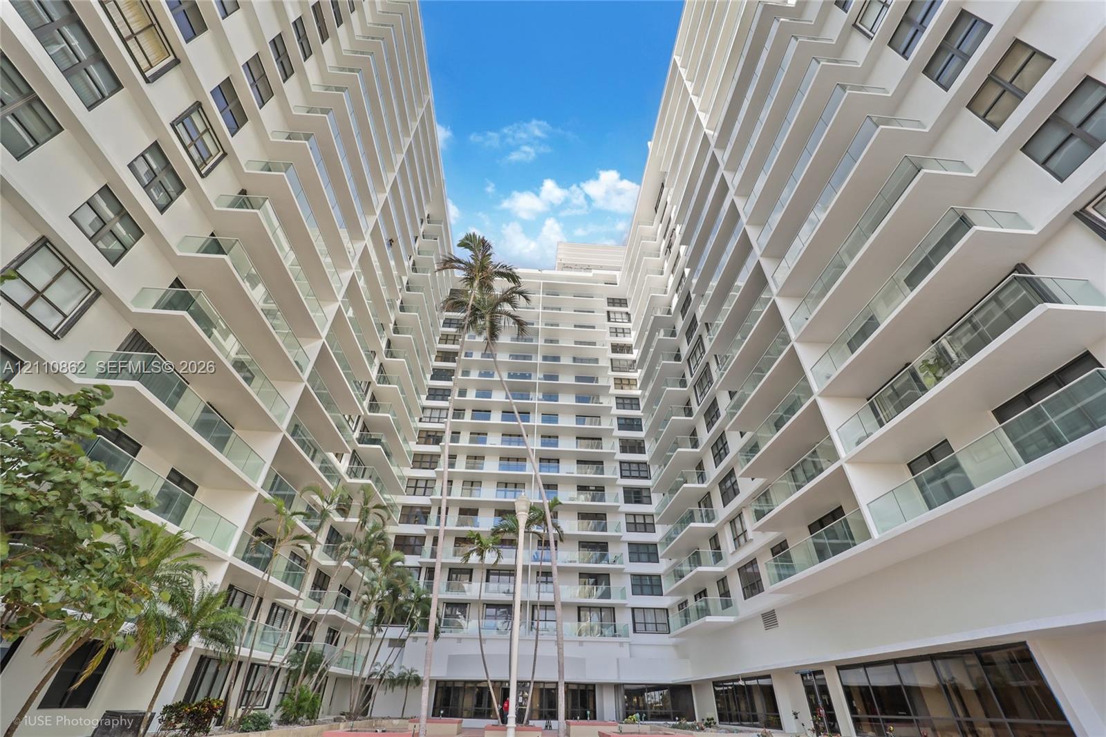 architecture featuring white structural siding, multiple stories of glass-railed balconies, and mature palm trees