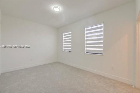 Neutral-toned carpeted flooring, white wall finishes, dual windows featuring adjustable banded roller shades, and a central flush-mount ceiling light fixture
