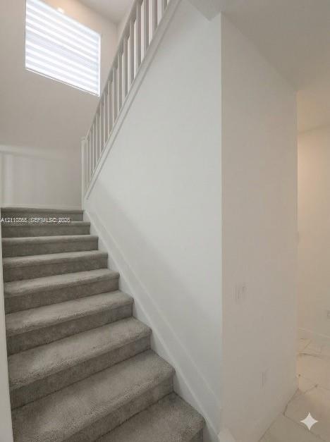 Staircase featuring neutral carpeting, white vertical balusters, and a high-reaching window with integrated blinds