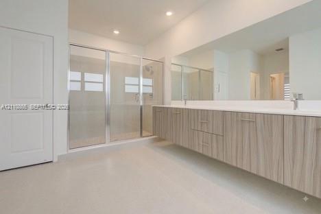 Floating dual-sink vanity with wood-grain cabinetry, expansive wall-to-wall mirror, and glass-enclosed shower with tiled surround