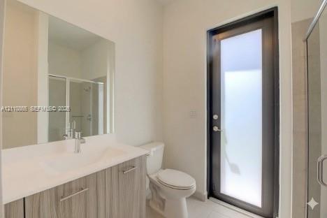 Bathroom featuring a vanity with a light wood-finish cabinet and solid surface countertop, an oversized wall-mounted mirror, a full-height glass-panel door, and a glass-enclosed shower