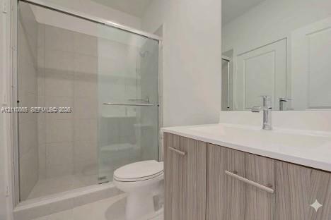 Bathroom featuring a vanity with a light wood-finish cabinet and an integrated countertop, a glass-enclosed shower with tiled surround, and a wall-mounted mirror