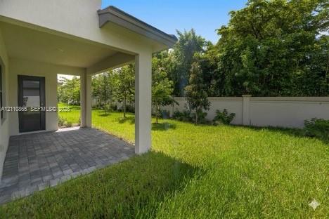 Covered patio with paver flooring, expansive lawn, and concrete privacy wall