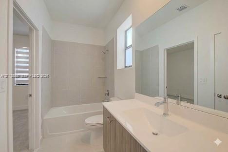 Bathroom featuring a wood-finish vanity with a white integrated sink, full-width wall mirror, and a tub-shower combination with floor-to-ceiling tile surround