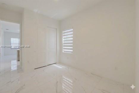 Neutral-toned interior featuring large-format tile flooring with a veined pattern, two-panel interior doors, and a window fitted with horizontal dual-layer shades