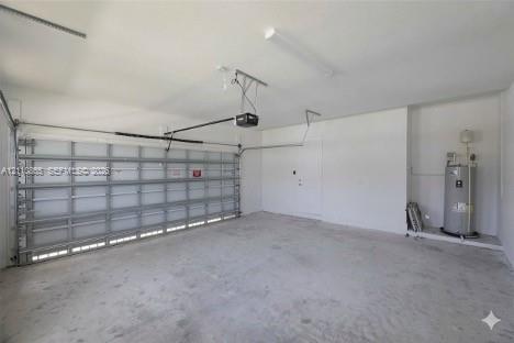 Multi-car garage featuring a concrete floor, sectional roll-up door, automated door opener, finished walls, and an integrated water heater