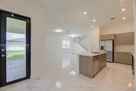 Open-concept interior featuring light-toned stone-finish flooring, recessed lighting, and a kitchen equipped with wood-finish cabinetry, a quartz-topped center island, and stainless steel appliances