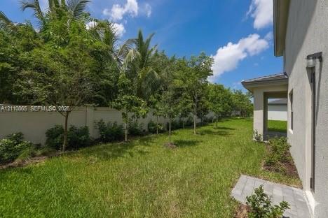 Side yard featuring a grass lawn, paved stone walkway, perimeter masonry wall, and mature landscaping