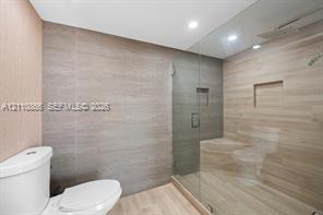 Walk-in shower featuring a frameless glass enclosure, recessed wall niche, and integrated bench seat, complemented by neutral-toned wall tiling and recessed lighting