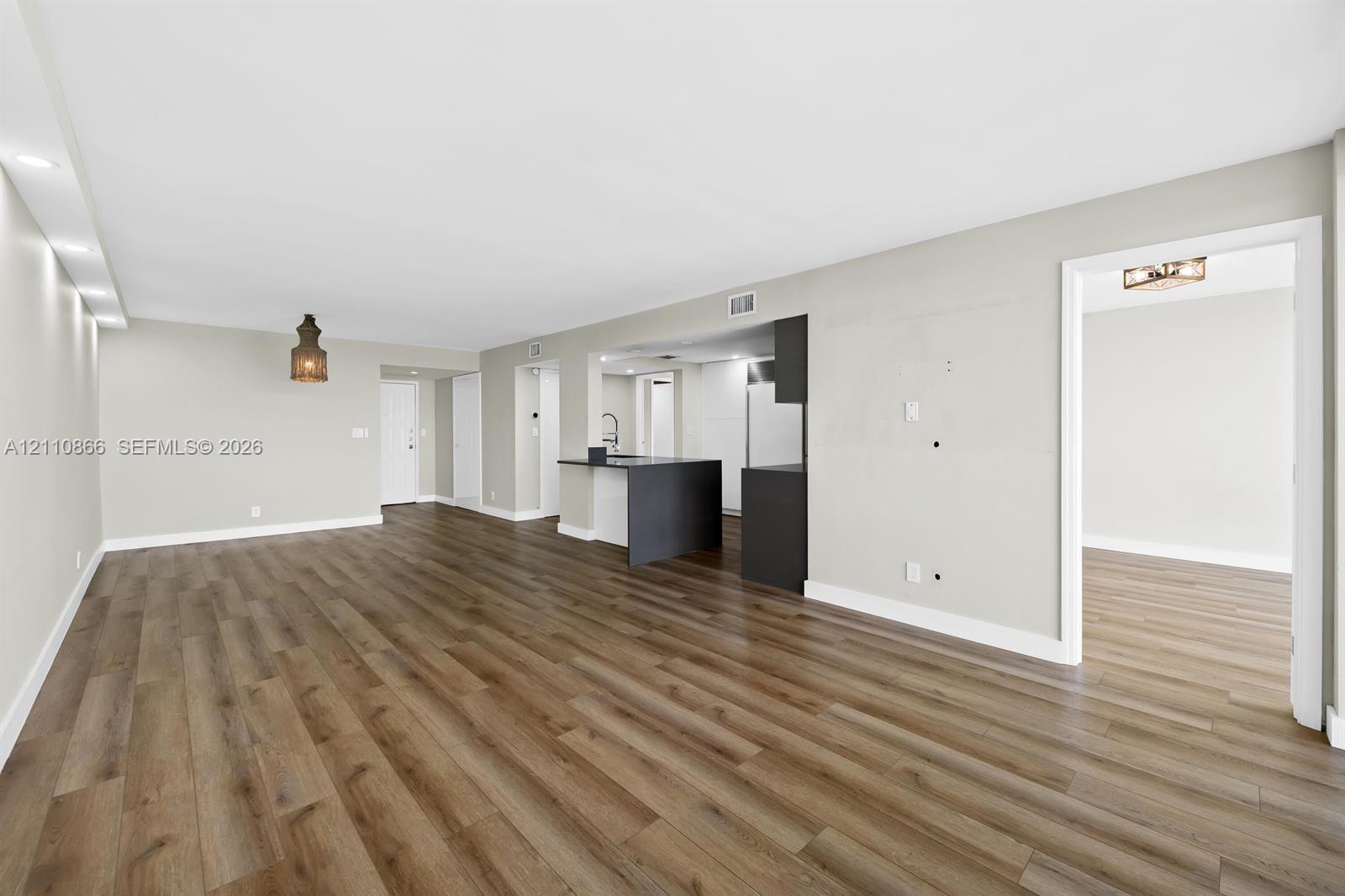 Open interior featuring wood-finish flooring, recessed lighting, and a kitchen peninsula with dark cabinetry Open interior featuring wood-finish flooring, recessed lighting, and a kitchen peninsula with dark cabinetry