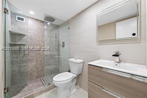 Bathroom featuring a floating vanity with dual drawers, integrated sink with a chrome waterfall faucet, walk-in shower with glass enclosure and stone-tile surround, and recessed lighting