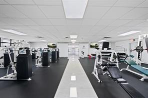 Fitness room featuring rubberized flooring, a center tile aisle, recessed fluorescent lighting, and wall-mounted televisions