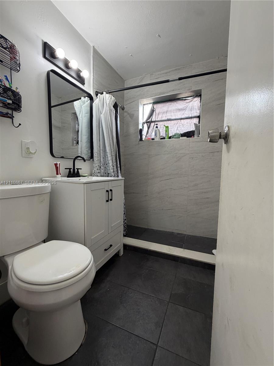 Bathroom featuring a white vanity cabinet, rectangular wall-mounted mirror, matte black fixtures, dark floor tile, and light-toned wall tile