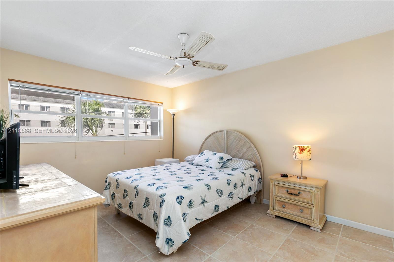 Neutral-toned interior space featuring light-colored tile flooring, wide-paneled window, and an integrated ceiling fan
