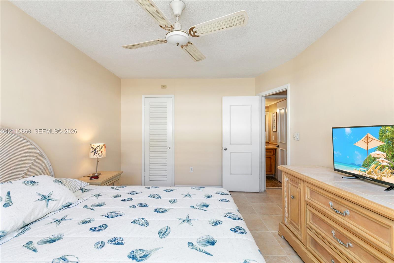 Interior room featuring neutral wall tones, large-format tile flooring, a white paneled door, a white louvered-style closet door, and a ceiling fan with integrated lighting