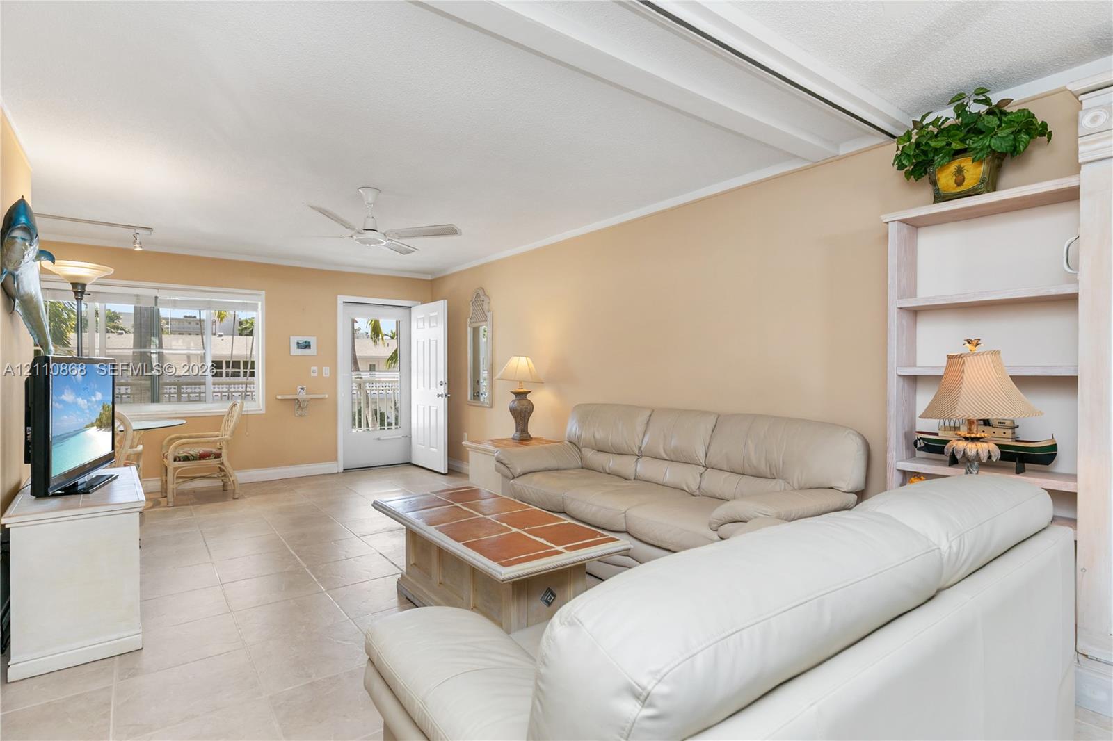Neutral tile flooring, built-in shelving unit, ceiling fan, and large windows providing natural light