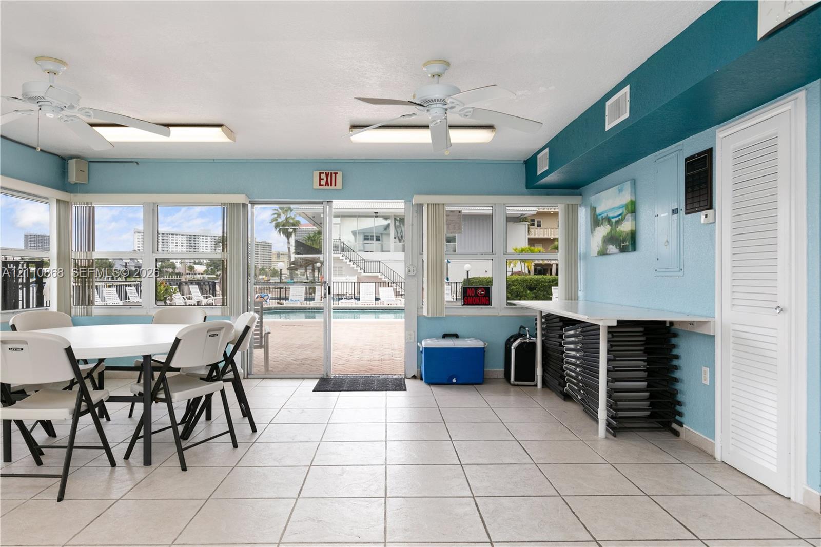 Large windows, neutral tile flooring, dual ceiling fans, and a sliding glass door providing access to the pool area