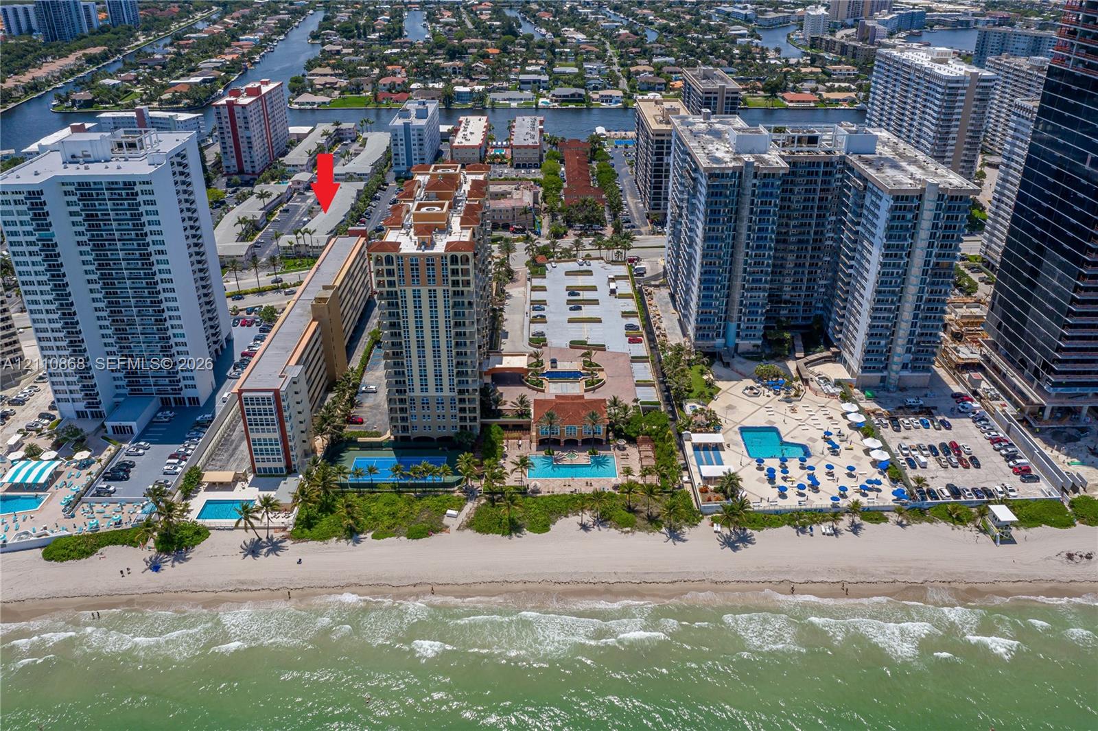Aerial coastal perspective featuring multiple high-rise residential structures, on-site swimming pools, tennis courts, and direct proximity to the ocean shoreline