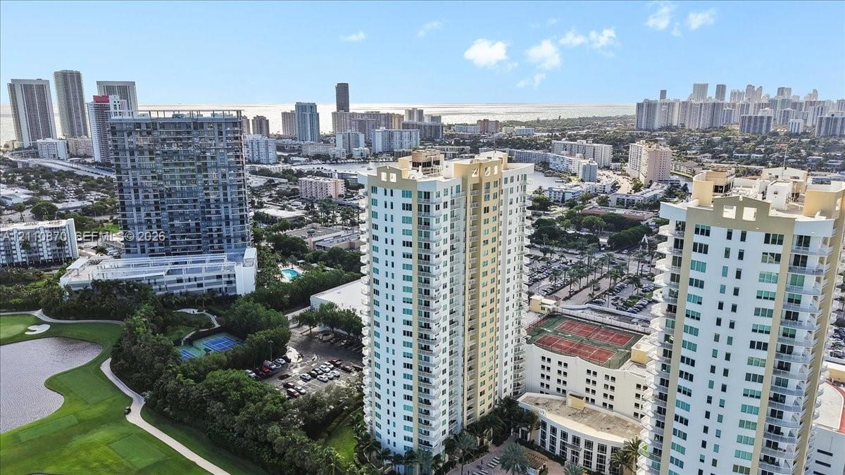 High-rise residential tower featuring wraparound balconies, multi-story glass-paned windows, tennis courts, and proximity to an expansive golf course