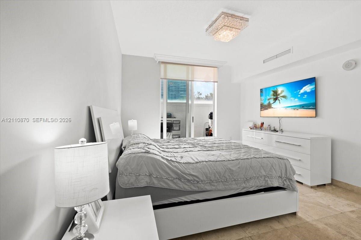 Neutral-toned room featuring stone flooring, a multi-tiered crystal flush-mount light fixture, and floor-to-ceiling glass sliding doors with a roller shade