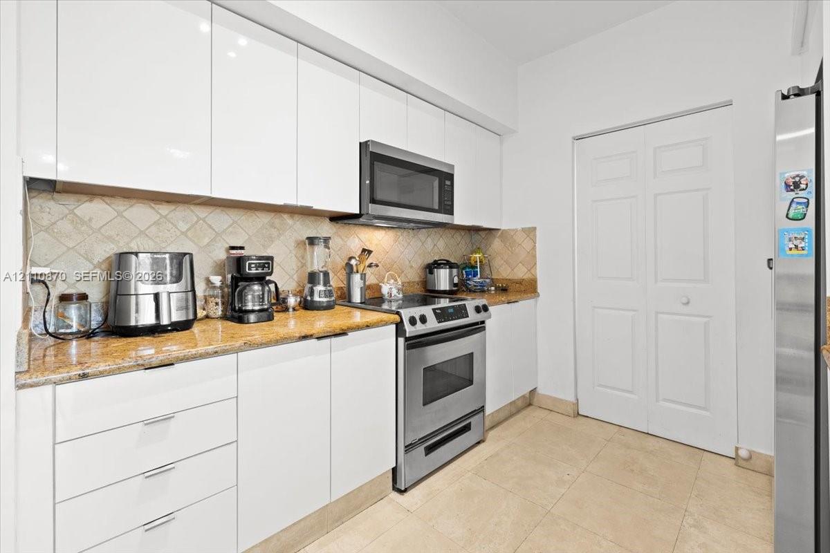 Kitchen featuring flat-panel white cabinetry, stone-finish countertops, stainless steel appliances, tiled backsplash, and tile flooring
