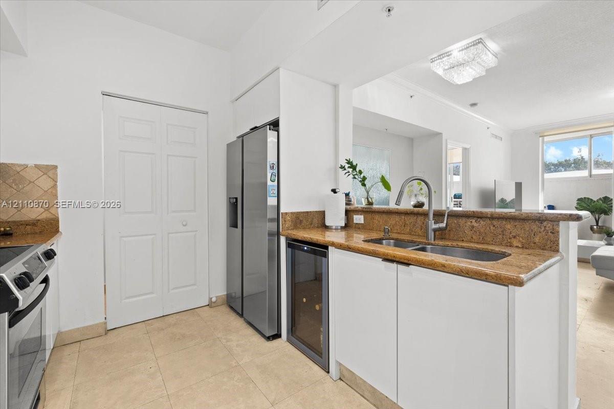Kitchen featuring stone countertops, integrated under-counter wine storage, stainless steel refrigerator, tile flooring, and double-basin undermount sink with gooseneck faucet