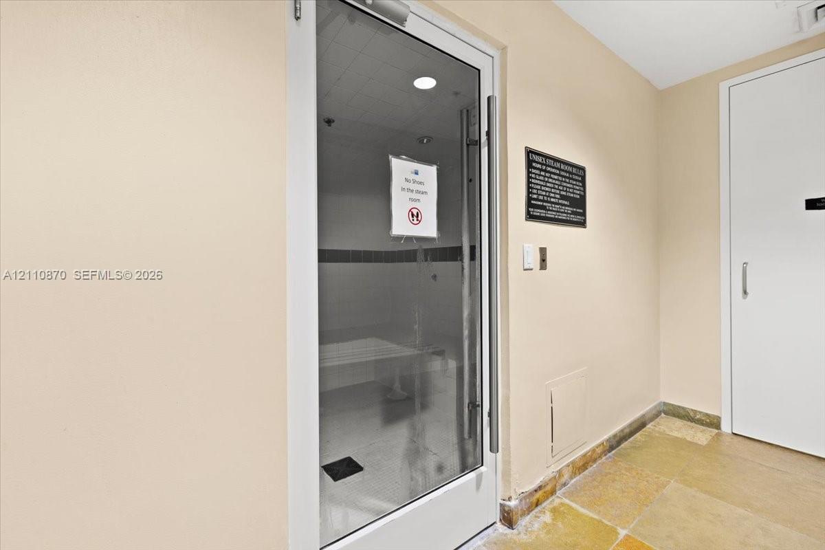Steam room featuring a glass-panel door, built-in bench seating, recessed lighting, and stone flooring