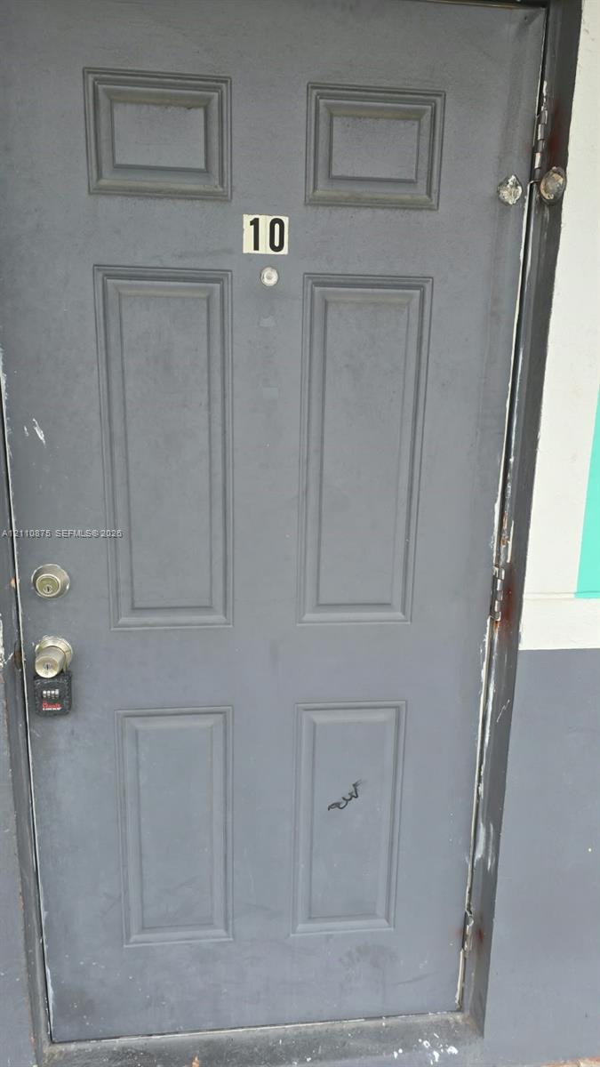 Gray six-panel entry door with integrated peephole, numerical signage, and metallic hardware