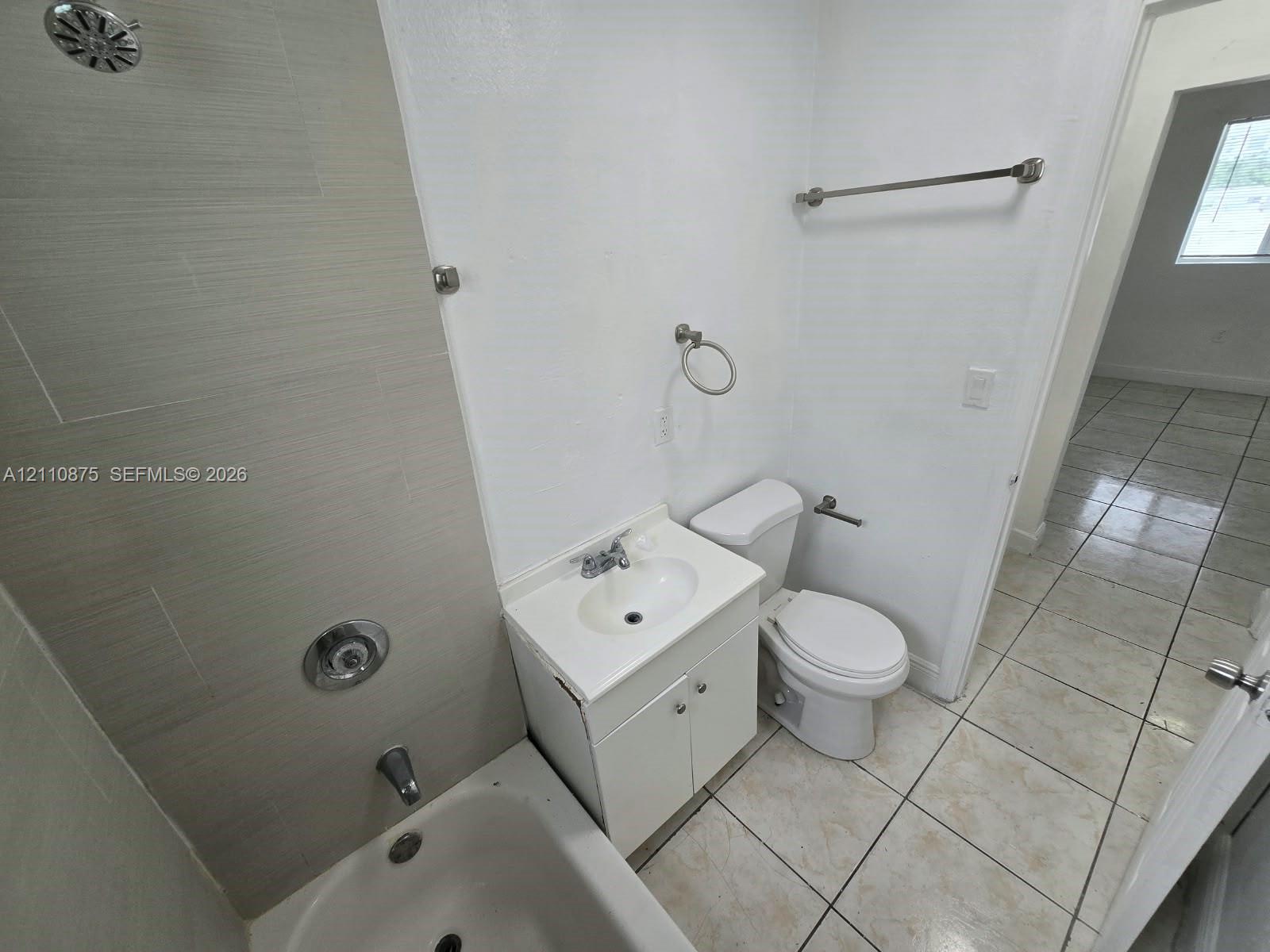 Bathroom featuring tile flooring, a tub-shower combination with light-toned wall tile, a white vanity with an integrated sink, and metallic fixtures