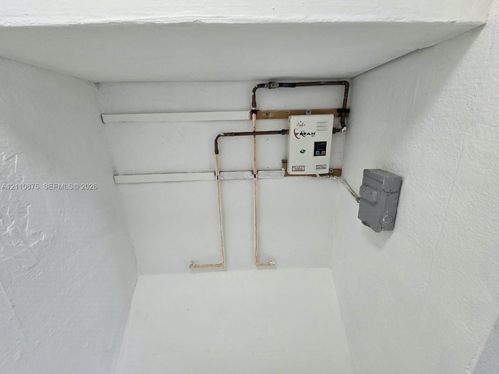 Tankless electric water heater featuring copper plumbing connections and a wall-mounted electrical disconnect switch