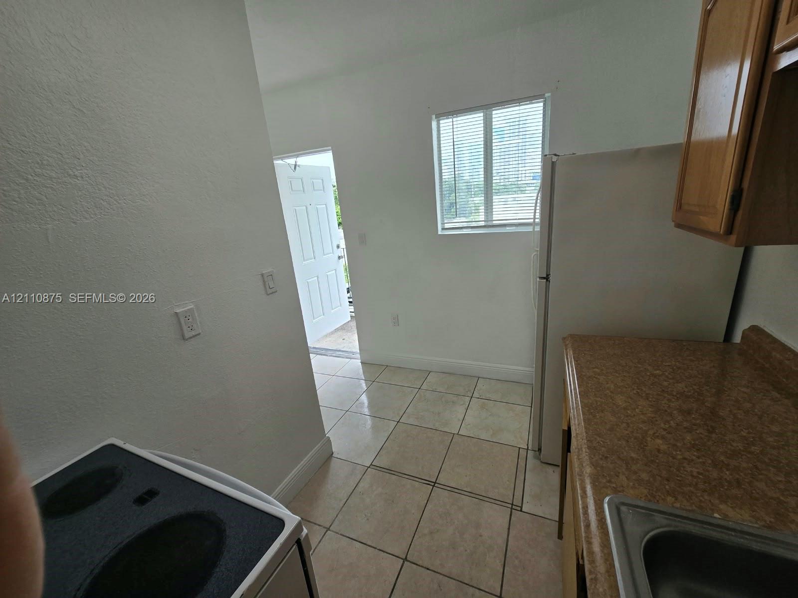 Kitchen featuring tile flooring, wood-finish cabinetry, a white refrigerator, an electric range, and a single-pane window