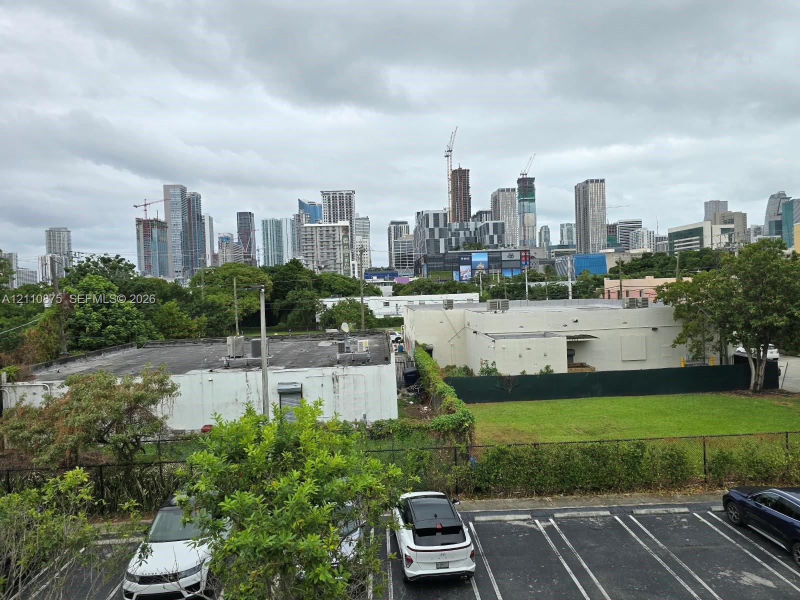 Urban landscape featuring a high-rise skyline, paved parking area, and open green space