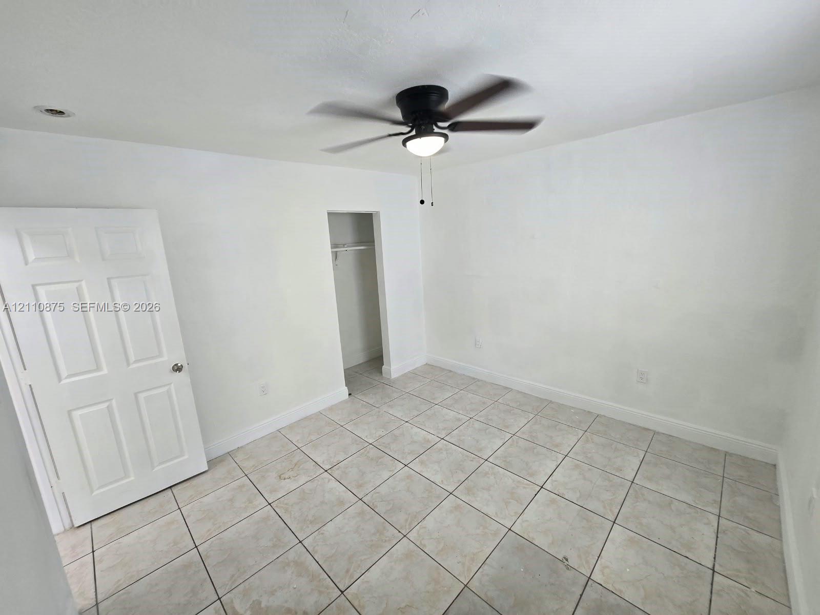 Interior space featuring light-colored tile flooring, a six-panel door, a walk-in closet, and a ceiling fan with integrated lighting