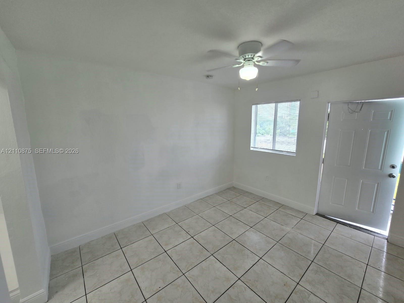 Interior space featuring large-format neutral floor tiling, a multi-blade ceiling fan with an integrated light fixture, a single-panel window, and a white six-panel exterior door