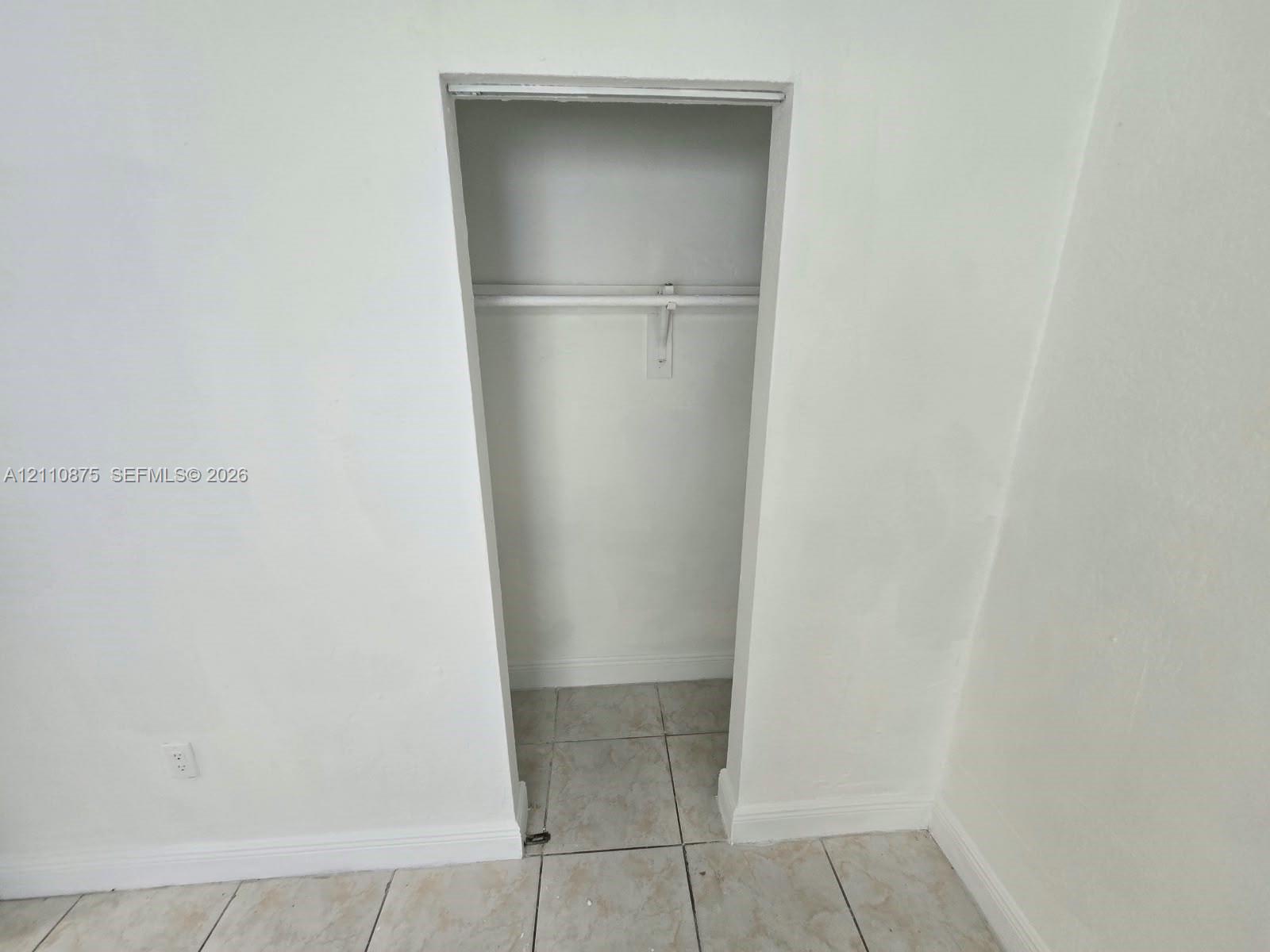 Built-in closet featuring a horizontal hanging rod and ceramic tile flooring
