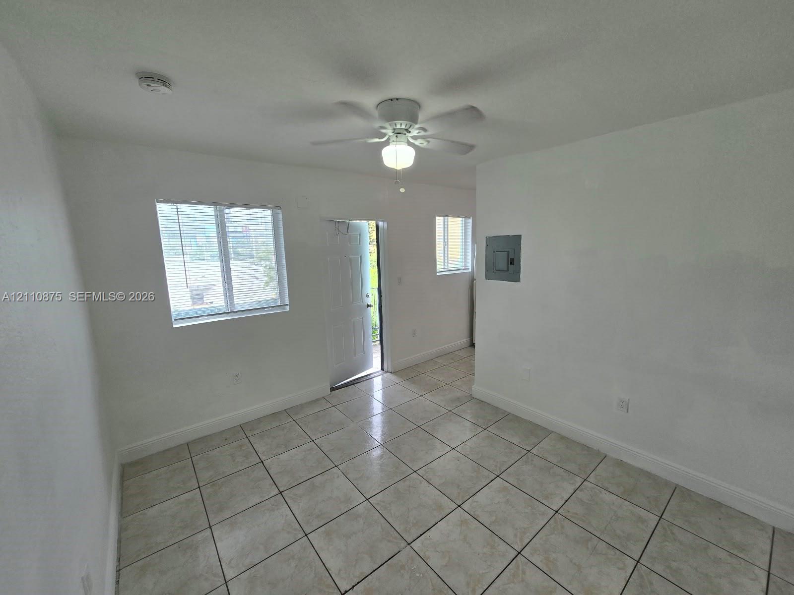 Interior space featuring neutral wall tones, large-format ceramic tile flooring, a ceiling-mounted fan with integrated lighting, and multiple windows providing natural illumination