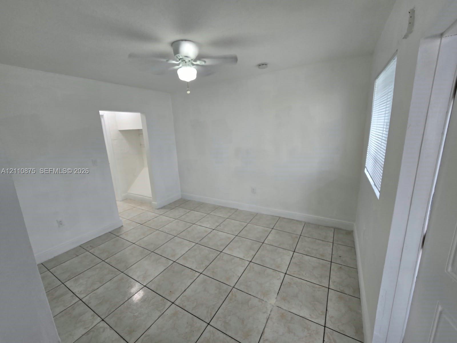 Neutral interior space featuring ceramic tile flooring, a white ceiling fan with integrated light fixture, and horizontal blind window treatments