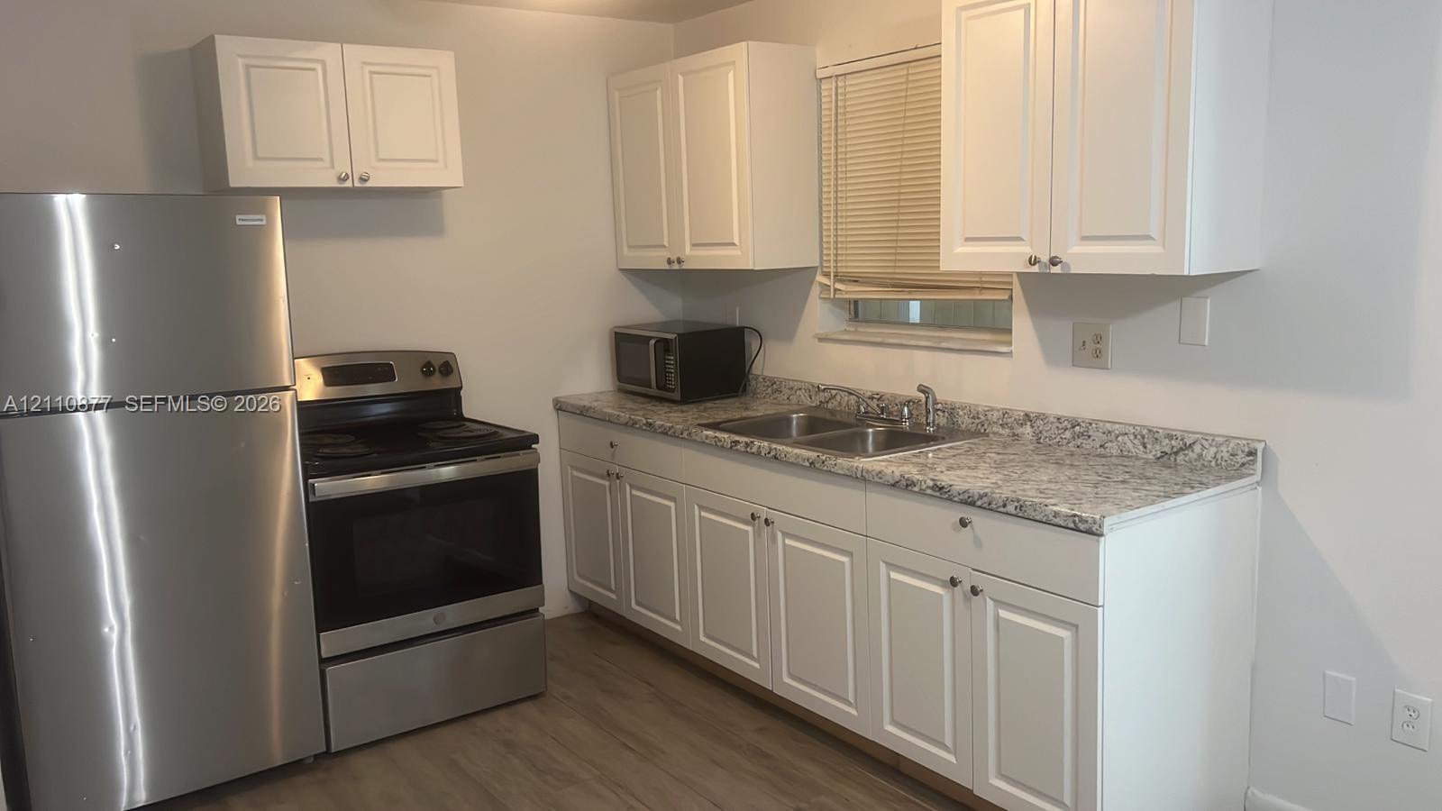 Kitchen featuring white shaker-style cabinetry, patterned stone-finish countertops, dual-basin stainless steel sink, and stainless steel appliances