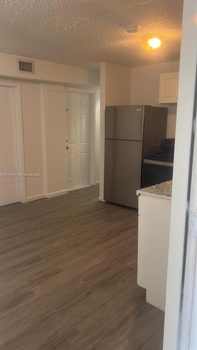 Wood-finish flooring, stone-surfaced countertops, white shaker-style cabinetry, and stainless steel refrigerator