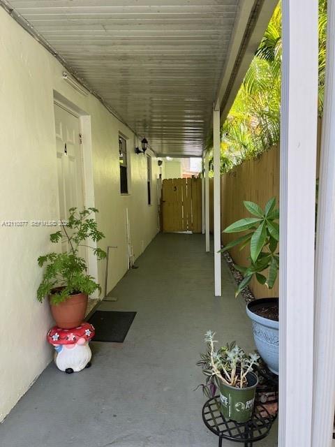 Covered exterior walkway featuring a concrete floor, support pillars, wall-mounted light fixture, and wooden privacy fencing