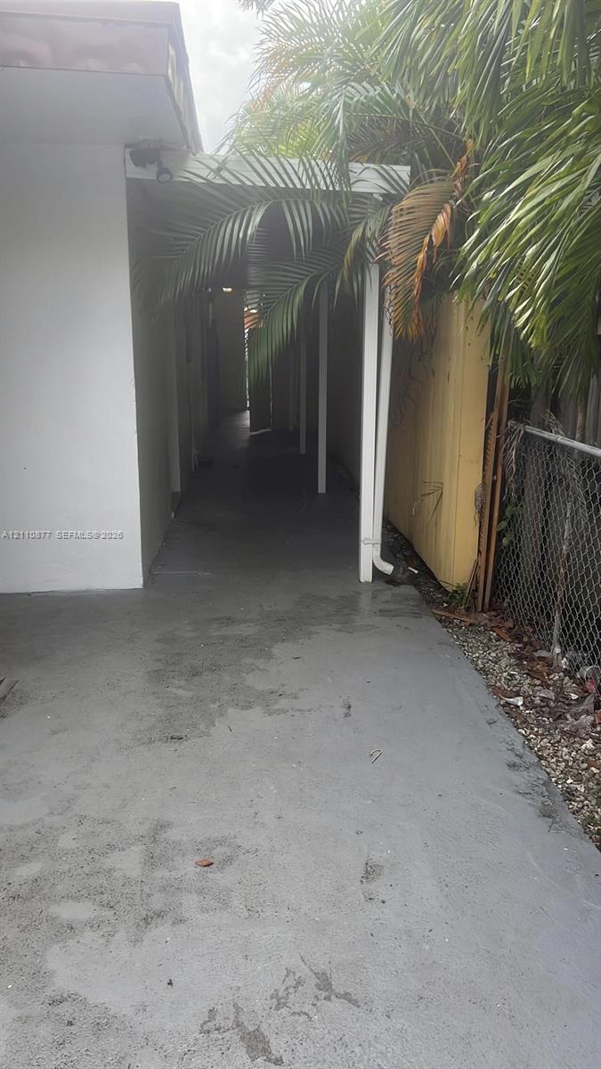 Covered exterior walkway featuring a concrete path, structural support posts, and perimeter fencing