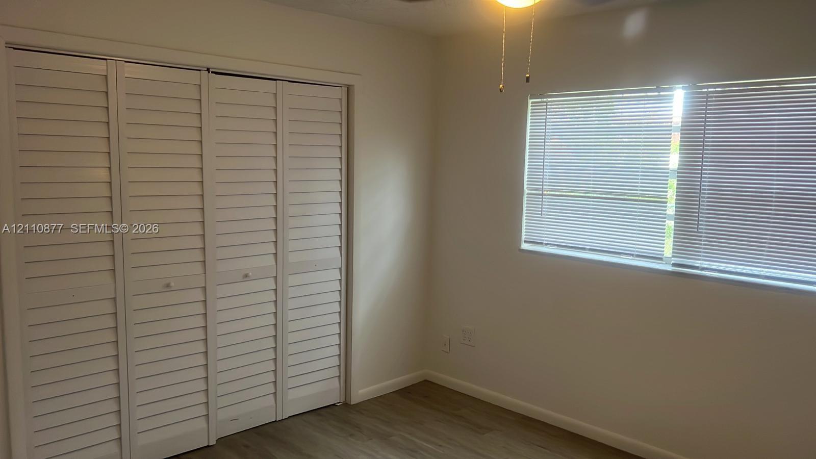 Room featuring four-panel louvered closet doors, wood-finish flooring, and a ceiling-mounted light fixture