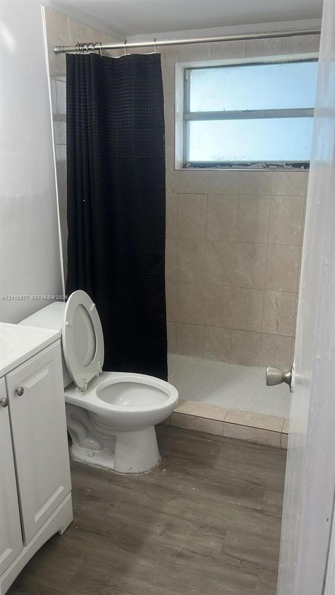 Bathroom featuring a white vanity cabinet, wood-finish flooring, and a walk-in shower with neutral wall tiling and an integrated window